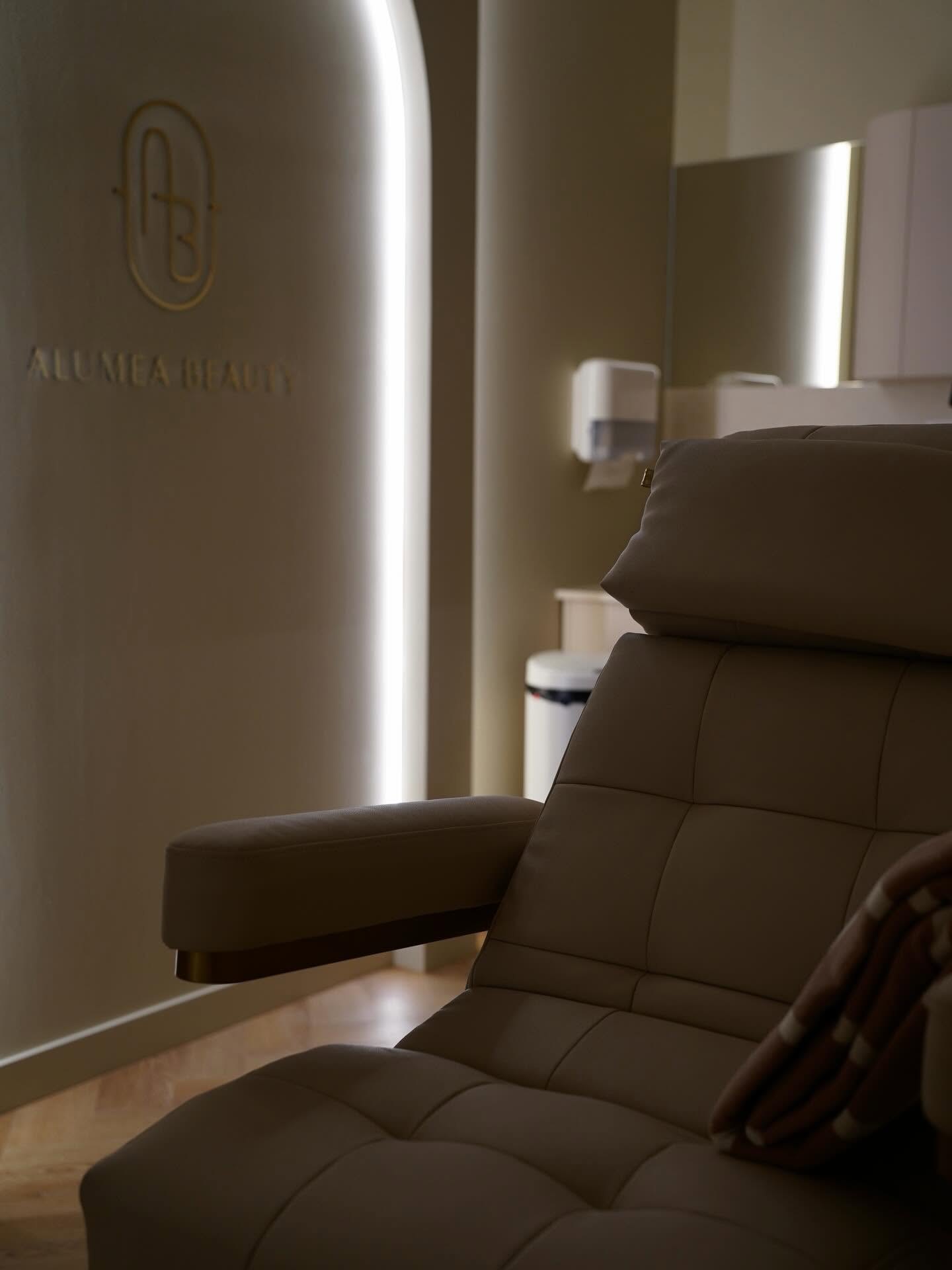 Gabinet zabiegowy Alumea Beauty: fotel, podświetlony łuk i złoty monogram na ścianie